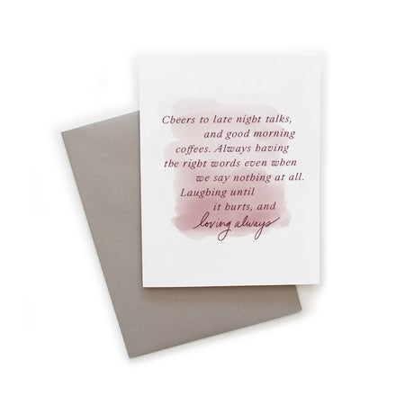 White card with blush pink muted brushstroke background with dark pink text saying, “Cheers to late night talks, and good morning coffees. Always having the right words even when we say nothing at all. Laughing until it hurts and loving always.” A gray envelope is included.