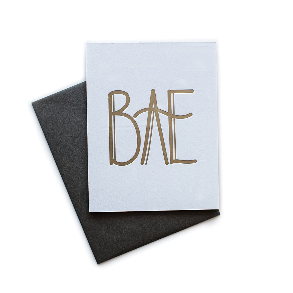 White card with gold text saying, “BAE”. A gray envelope is included.