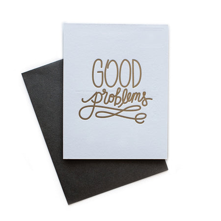 White card with gold text saying, “Good Problems”. A gray envelope is included.