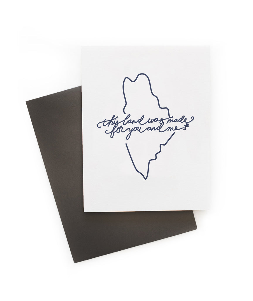 White card with blue text saying, “This Land is Made for You and Me”. Blue outline image of the state of Maine. A gray envelope is included.