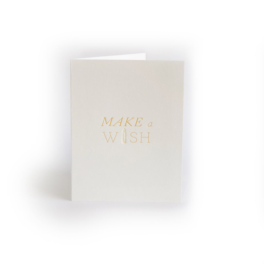 Ivory card with gold text saying, “Make a Wish”. Image of a birthday candle. A gray envelope is included.