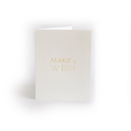 Ivory card with gold text saying, “Make a Wish”. Image of a birthday candle. A gray envelope is included.