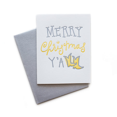 White card with gray and yellow text saying, “Merry Christmas Y’All”. Images of a pair of yellow cowboy boots. A gray envelope is included.