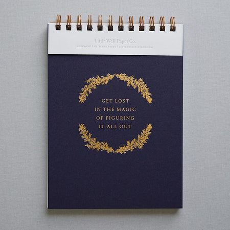 Navy blue notebook with gold text saying, “Get Lost in the Magic of Figuring It All Out”. Brass coil binding across the top.