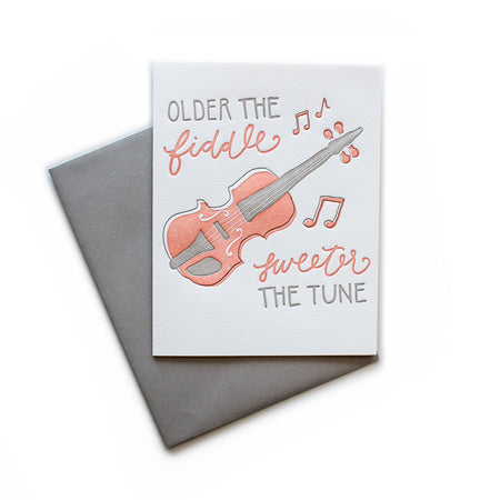 White card with gray and red text saying, “Older the Fiddle Sweeter the Tune”. Images of a red fiddle with red music notes. A gray envelope is included.