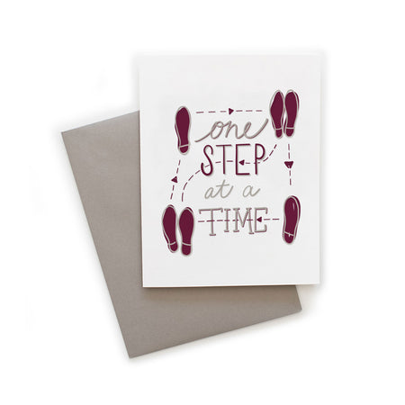 White card with gray and red text saying, “One Step at a Time”. Image of shoeprints making a square in the direction of the box-step dance. A gray envelope is included.