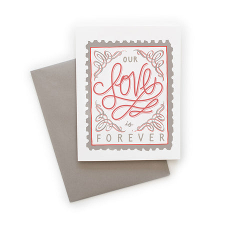 White card with gray and red text saying, “Our Love is Forever”. Image of a postage stamp with LOVE written in script in red across middle of card. A gray envelope is included.