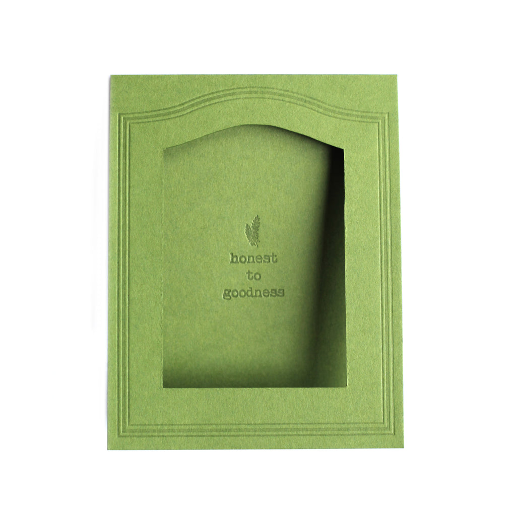Rectangle green card with arched photo cut out in center with text saying, “Honest to Goodness” with an embossed image of a green fern.  A matching envelope is included.