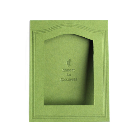 Rectangle green card with arched photo cut out in center with text saying, “Honest to Goodness” with an embossed image of a green fern.  A matching envelope is included.