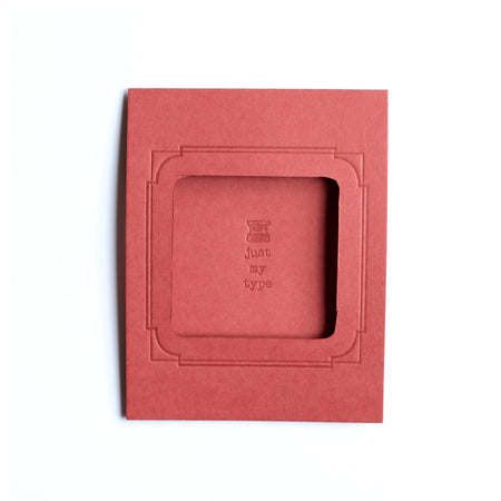 Rectangle red card with arched photo cut out in center with text saying, “Just My Type” with embossed image of a typewriter. A matching envelope is included.