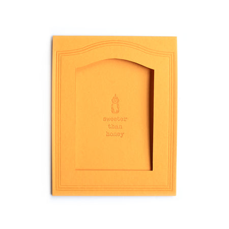 Rectangle mustard yellow card with arched photo cut out in center with text saying, “Sweeter Than Honey” with an embossed image of a squeezable bottle of honey.  A matching envelope is included.