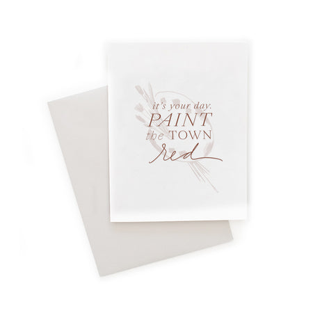 White card with red text saying, “It’s Your Day Paint the Town Red”. Image of an artist pain palette and paintbrushes. A gray envelope is included.