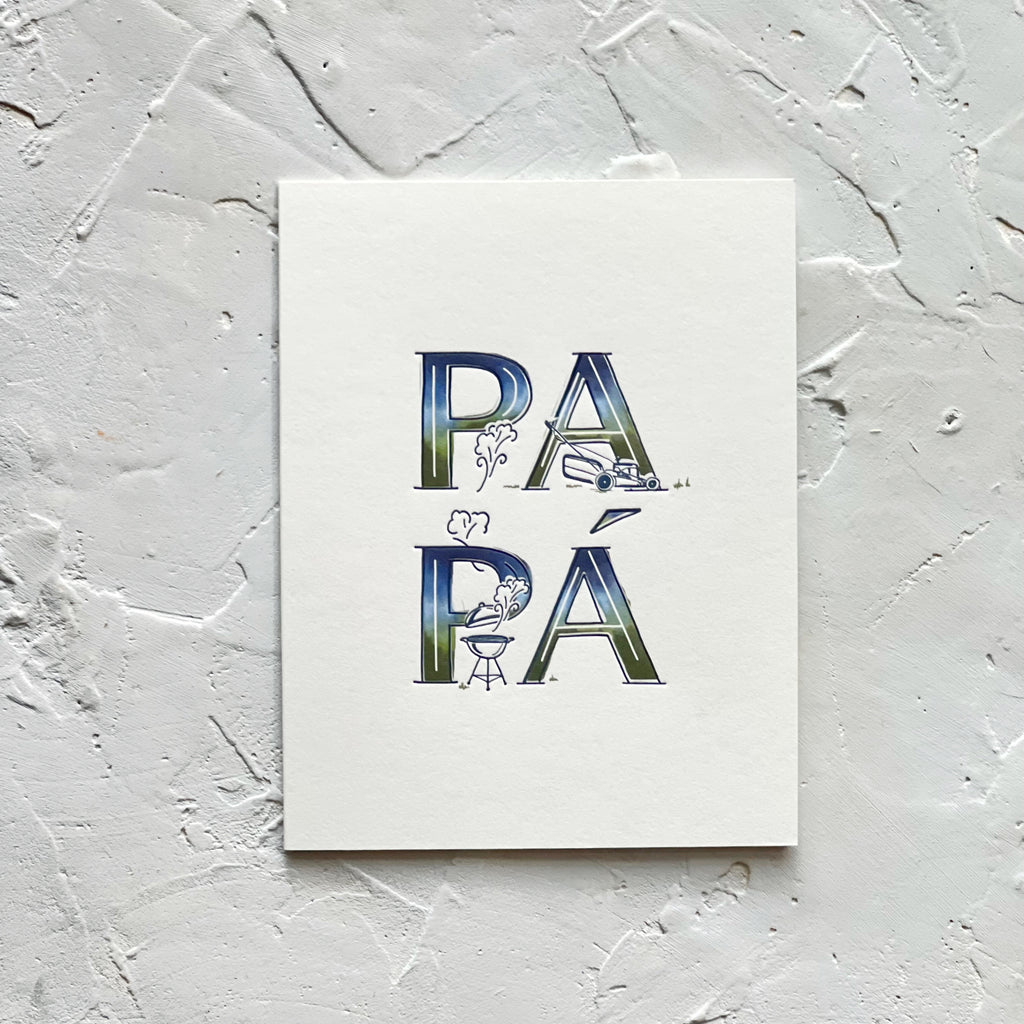 White card with variegated colored text in blue, green, and white saying, “PAPA”. Images of a lawn mower and a bbq grill. A white envelope is included.