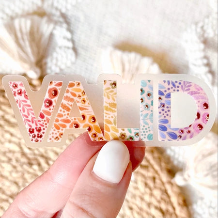 Multicolored pride sticker saying, “VALID”. Images of floral leaves on each letter.