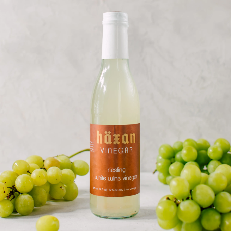 Large glass bottle with white lid and orange label with white and orange text saying, “Haxan Vinegar Riesling White Wine Vinegar”. Liquid is a white color.
