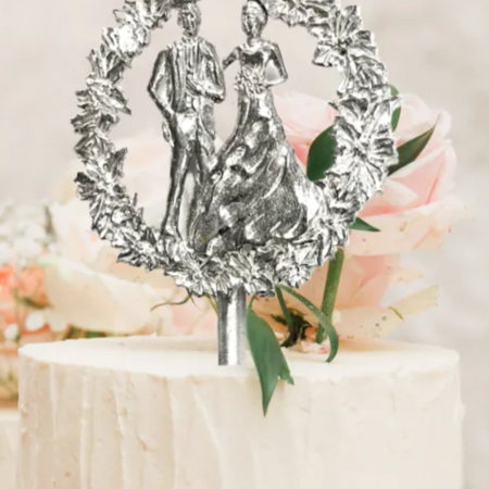 Silver pewter cake topper in the image of a bride and groom surrounded by a circle floral wreath.