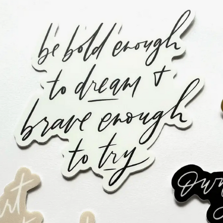 White sticker with black script text saying, “Be Bold Enough to Dream and Brave Enough To Try”. 