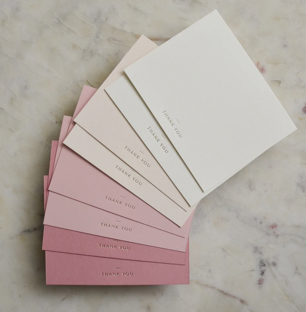 Notecards in ivory shades and pink shades with gold foil text saying, 