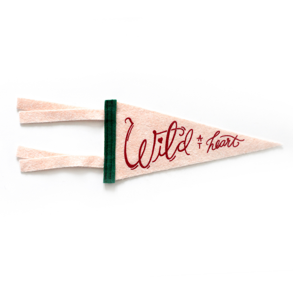 Peach flag pennant with red text saying, “Wild at Heart”. Vertical black band on left side of pennant.