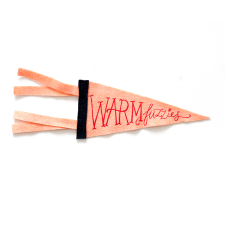 Peach background flag pennant with red text saying, “Warm Fuzzies”. Black vertical band on left side of pennant.
