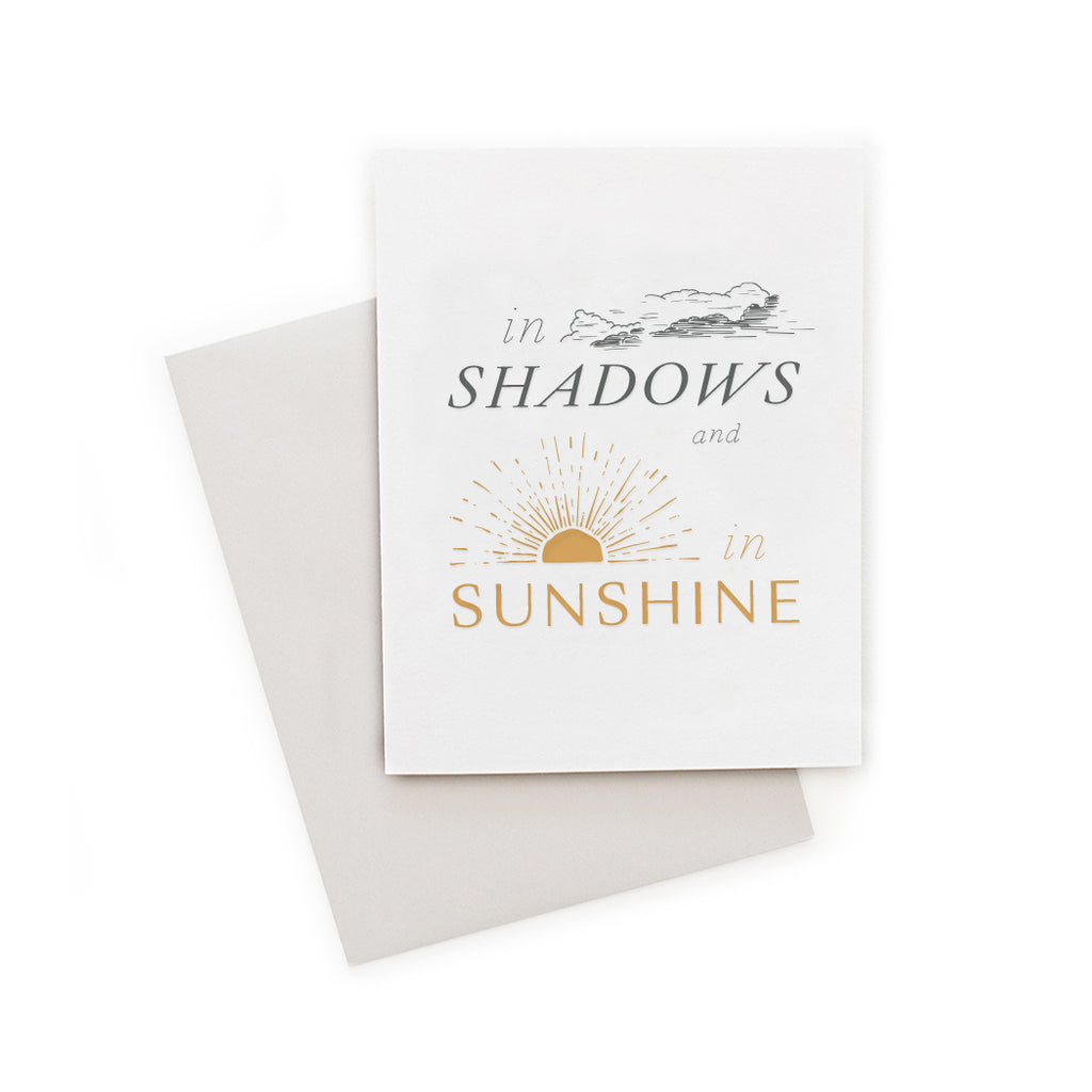 Ivory card with gray and yellow text saying, “In Shadows and In Sunshine”. Images of gray clouds and yellow sunshine. A gray envelope is included.