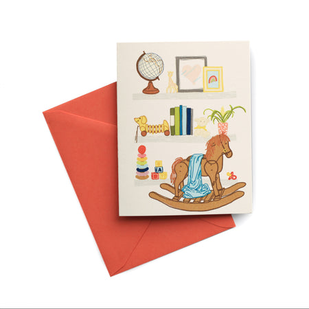 Ivory card with images of items found in a baby nursery: rocking horse, blocks, stackable rings, books, globe, plant, pull toy, giraffe and drawings. A red envelope is included.