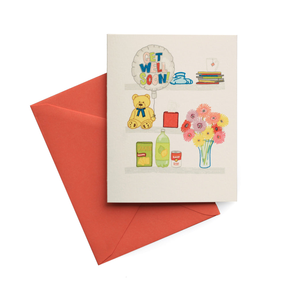 Ivory card with images of items needed when you are sick: books, hot tea, a vase of flowers; can of soup, ginger ale soda, saltine crackers; a teddy bear, Get Well balloon and a hot water bag. A burnt orange envelope is included.