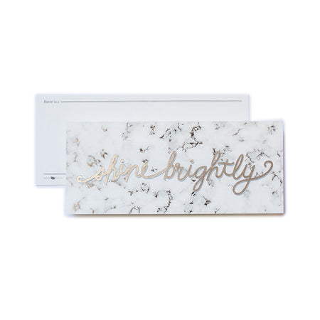 White rectangle card with black marbled background and gold text saying, “Shine Brightly”. An olive green envelope is included.
