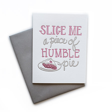 White card with gray and red text saying, “Slice Me A Piece of Humble Pie”. Images of a slice of red cherry pie on a plate. A gray envelope is included.