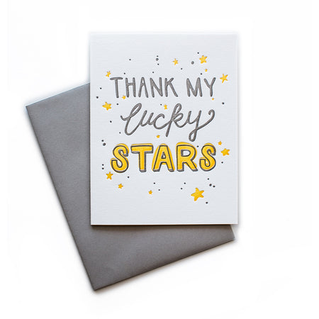 White card with gray and yellow text saying, “Thank My Lucky Stars”. Images of yellow stars and gray dots. A gray envelope is included.