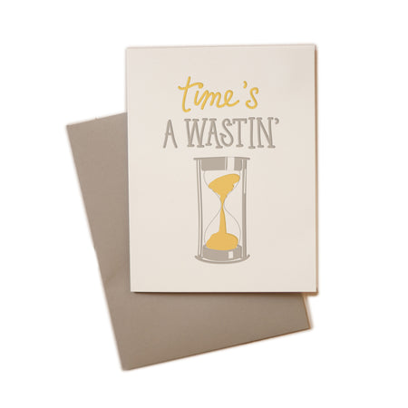 White card with gray and yellow text saying, “Time’s A Wastin’”. Image of a gray and yellow hourglass. A gray envelope is included.