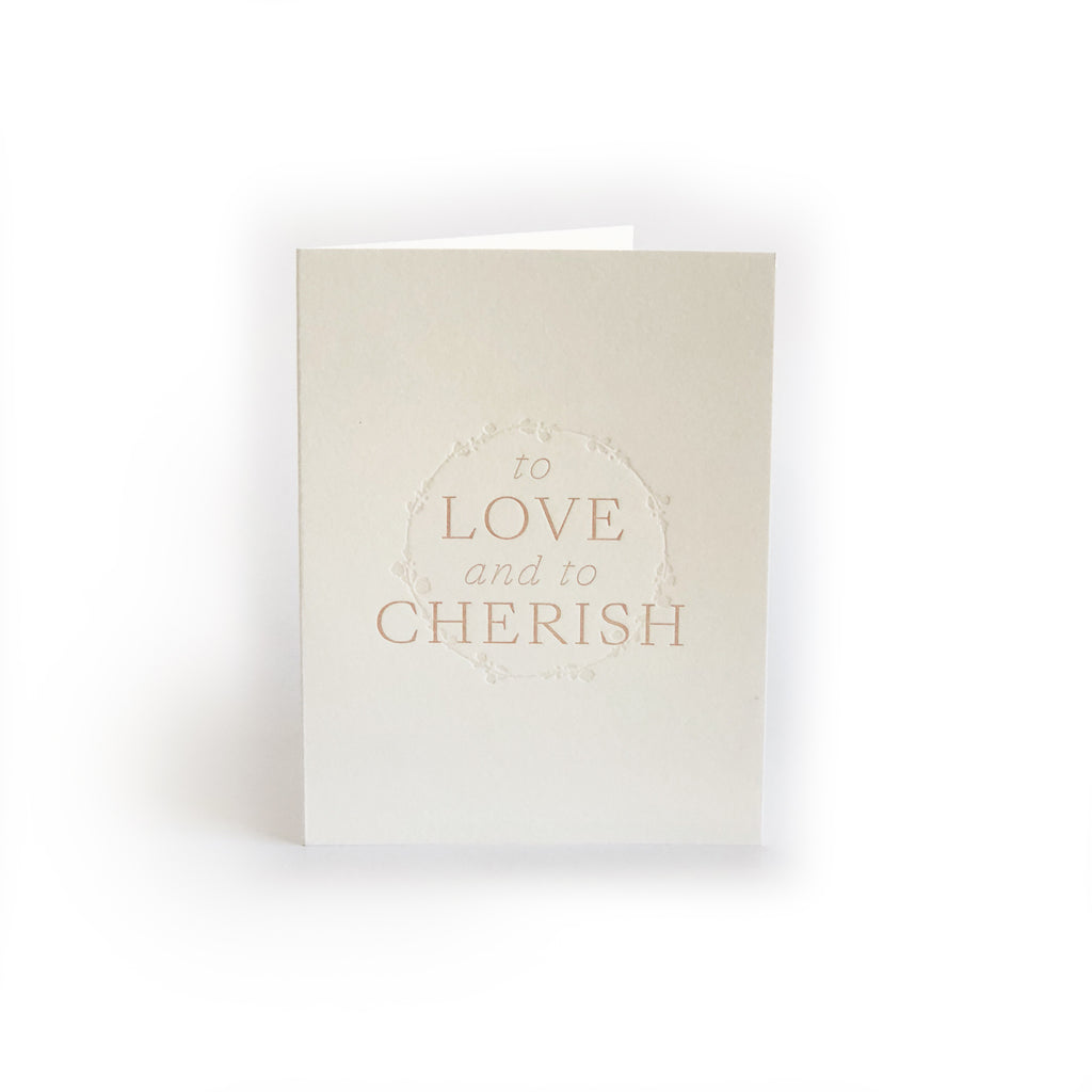 Ivory card with brown text saying, “To Love and to Cherish”. Images of embossed floral wreath ring. A gray envelope is included.