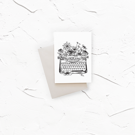 White card with black ink. Images of a vintage typewriter and flowers. A gray envelope is included.