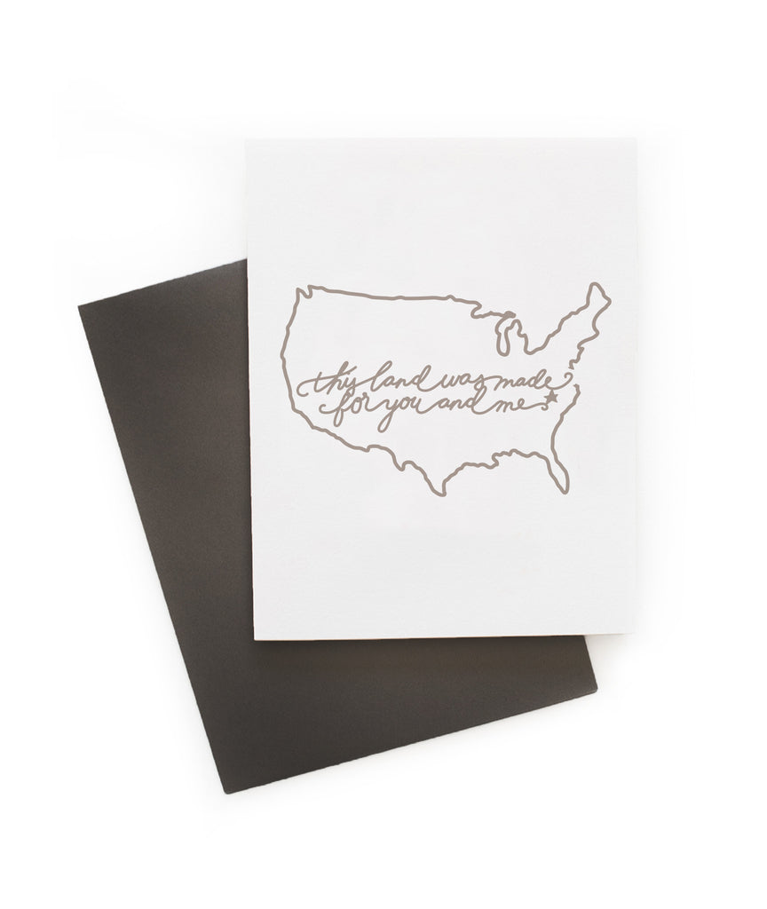 White card with black text saying, “This Land is Made for You and Me”. Black outline image of the United States. A gray envelope is included.