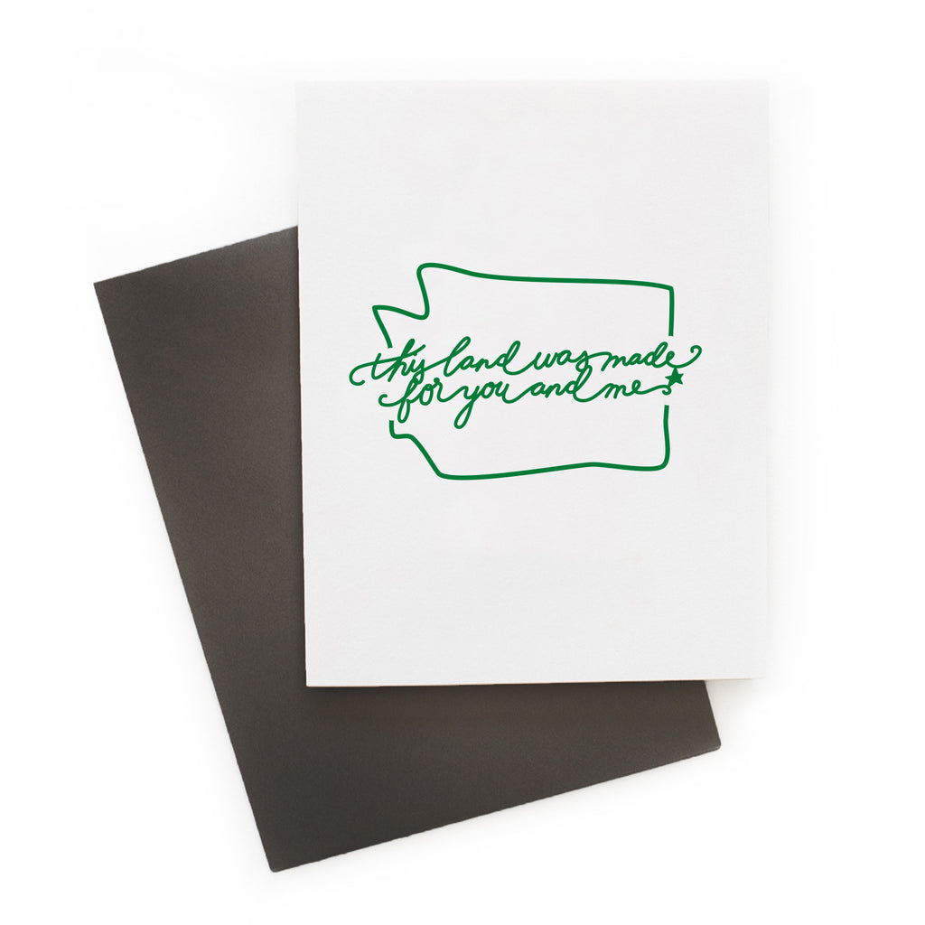 White card with green text saying, “This Land is Made for You and Me”. Green outline image of the state of Washington. A gray envelope is included.