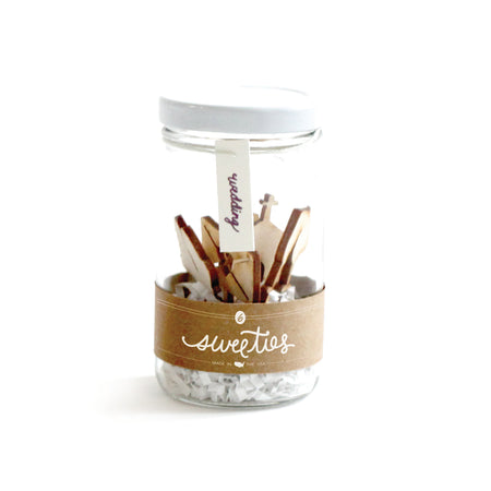 Wooden cutout cupcake picks in the images of wedding bells, ring, top hat, church, champagne glasses, and a love letter. Packaged in a glass jar with white lid and gold label.