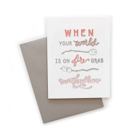 White card with gray and red text saying, “When Your World is on Fire Grab Marshmallows”. Images of sticks with marshmallows on the end. A gray envelope is included.