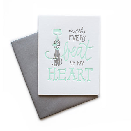 White card with gray and teal text saying, “With Every Beat of My Heart”. Image of a gray and teal hand egg beaters. A gray envelope is included.