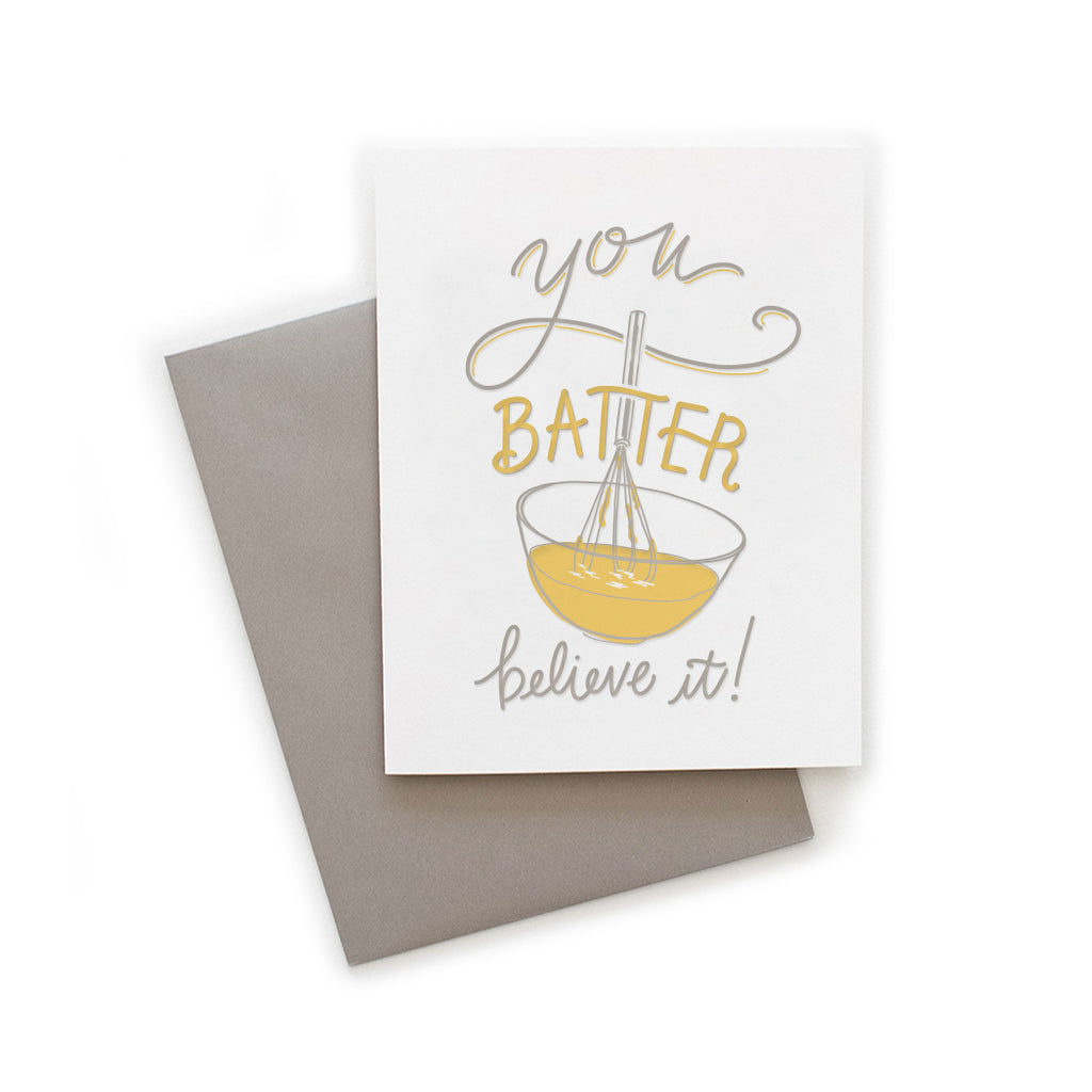 White card with gray and yellow text saying, “You Batter Believe It”. Image of a mixing bowl with yellow batter and gray wire whisk. A gray envelope is included.