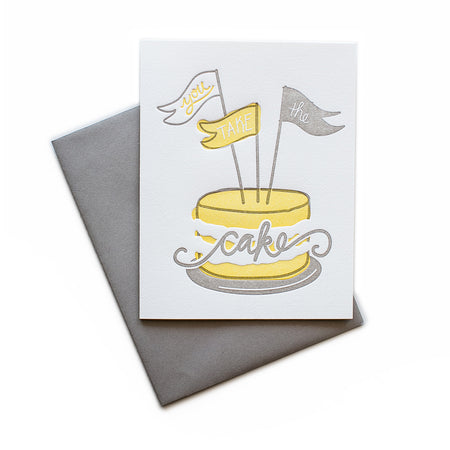 White card with gray and yellow text saying, “You Take the Cake”. Image of a gray and yellow cake with three flag pennants. A gray envelope is included.
