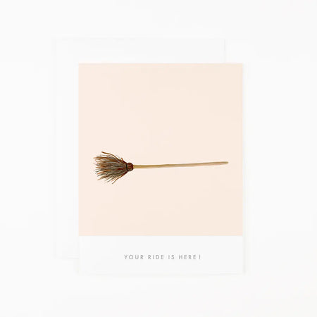Ivory card with green text saying, “Your Ride is Here”. Image of a brown matchstick broom. A white envelope is included.