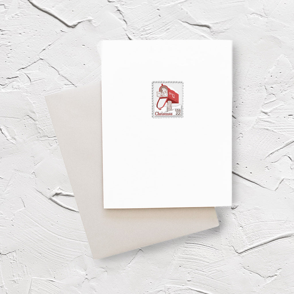 White card with image of a postage stamp with a red mailbox with packages poking out. Red text saying, “Christmas” and black text saying, “US22”. An ivory envelope is included.