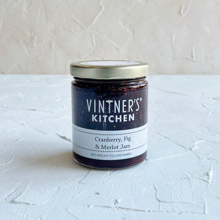 Glass jar with metal lid. White text saying, “Vintner’s Kitchen Cranberry, Fig & Merlot Jam”.