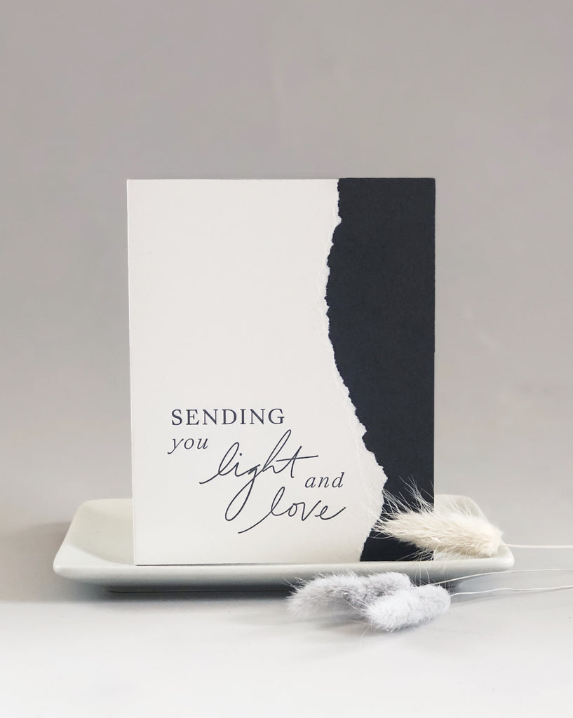 White and blue card with curved torn edging where the two colors meet. Blue text saying, “Sending You Light and Love”. A white envelope is included.