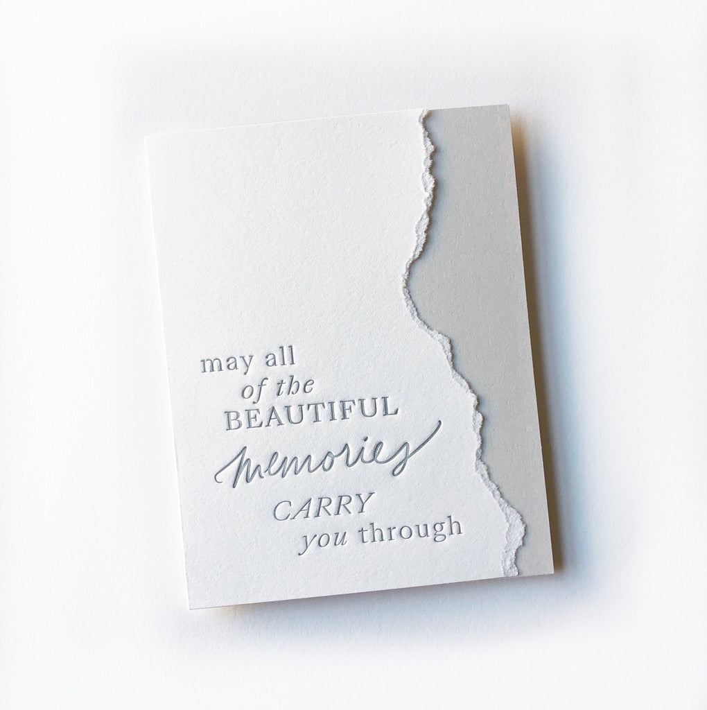 White card with torn edging and silver text saying, “May All of the Beautiful Memories Carry You Through”. An envelope is included.