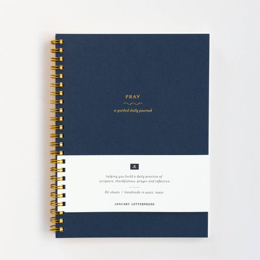 Navy blue cover with gold foil text saying, “Pray A Guided Daily Journal”. Gold coil binding on left side.