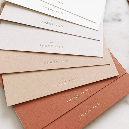 Notecards in ivory shades and orange shades with gold foil text saying, 